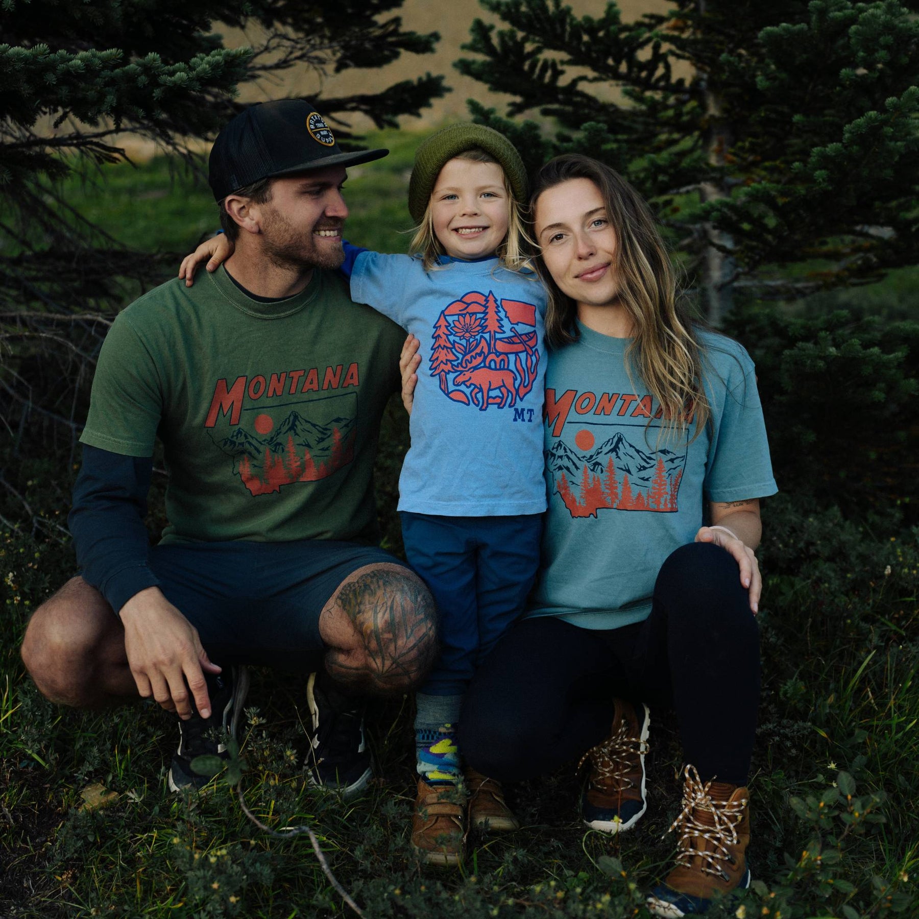 Kid wearing the Montana Nature Circle youth tee standing between two adults in Montana tees